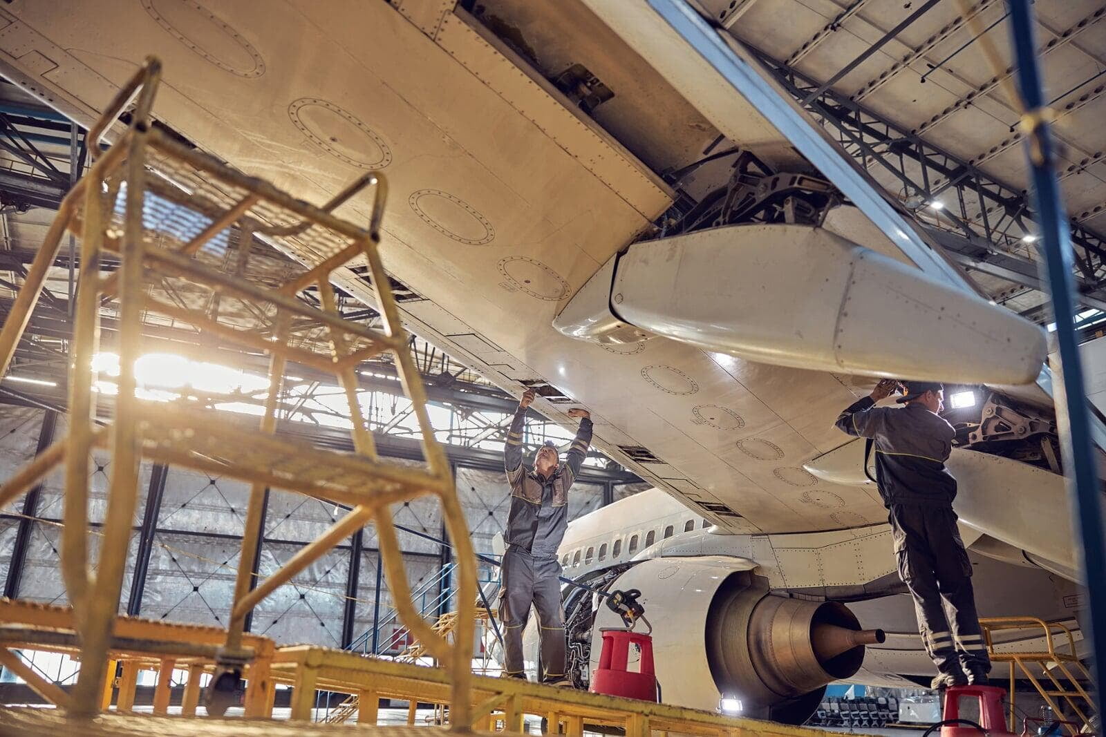 Deux ouvriers travaillent sous une aile d'avion.